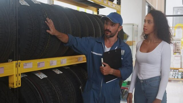 Customer woman choice tire wheel for car at the garage store with mechanic advise, auto service, female purchase wheel for vehicle, employee man advice about tyre and sell, transportation concept.