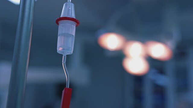 Medicine dripping during surgery. Intravenous dropper in surgery room on blurred background of medical lamp. Dropper during surgical operation in clinic. Close-up.