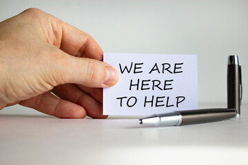 Help and support symbol. White paper with words 'we are here to help' in businessman hand, metalic pen. Beautiful white background. Business, help and support concept. Copy space.