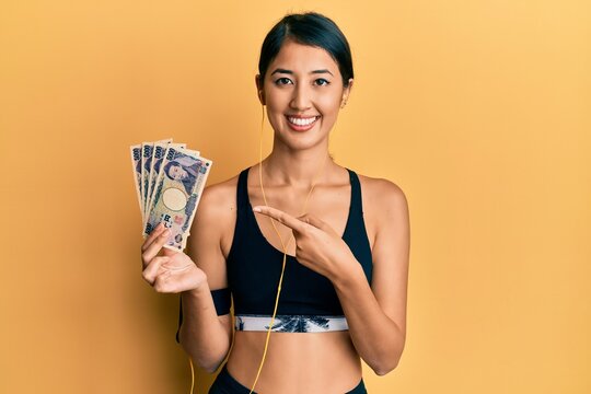 Beautiful asian young sport woman holding 5000 japanese yen banknotes smiling happy pointing with hand and finger