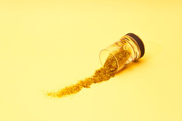 Spilled vodka glass full of gold glitter on golden yellow sunlit background. Minimal creative party and wealth concept.