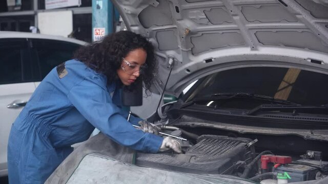 Young woman is mechanic repairing engine of car in the garage, auto service, worker fix and adjusting part of automobile with problems in the station, transportation and automotive concept.