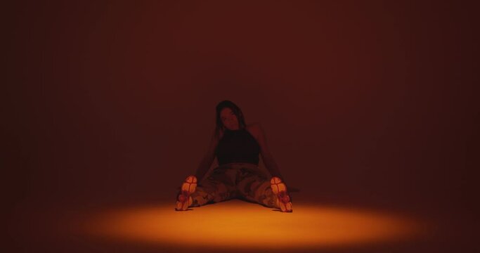 Girl sitting swinging feet on the dance floor in spotlight in studio. Taking a break to rest or waiting. Copy space