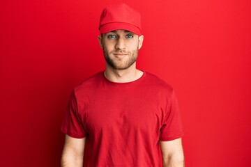 Young caucasian man wearing delivery uniform and cap with serious expression on face. simple and natural looking at the camera.