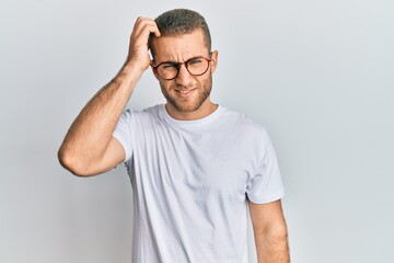 Young caucasian man wearing casual clothes and glasses confuse and wonder about question. uncertain with doubt, thinking with hand on head. pensive concept.