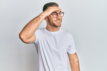 Young caucasian man wearing casual clothes and glasses very happy and smiling looking far away with hand over head. searching concept.