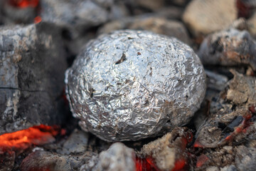 baked potatoes in foil in coals close up