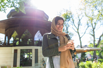 Muslim woman with hijab typing on her phone outside. 