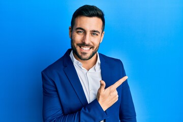 Young hispanic businessman wearing business jacket cheerful with a smile of face pointing with hand...