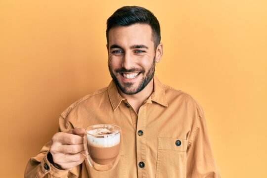 Handsome hispanic man enjoying a cup of coffee over yellow background