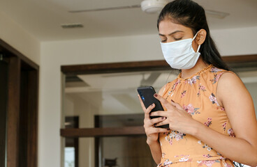 Closeup shot of an Asian girl wearing a mask and looking at her phone - new normal concept