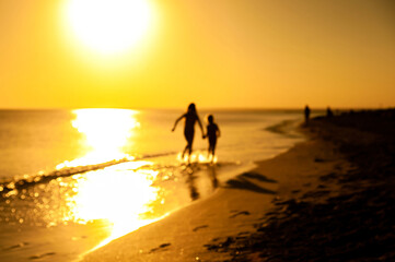 Silhouettes of two happy children playing and running along the seashore at sunset