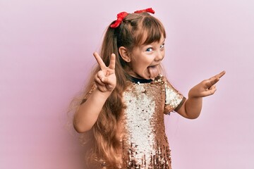 Little caucasian girl kid wearing festive sequins dress smiling looking to the camera showing fingers doing victory sign. number two.