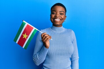 Young african american woman holding suriname flag looking positive and happy standing and smiling...