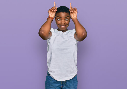 Young african american woman wearing casual white t shirt doing funny gesture with finger over head as bull horns