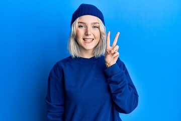 Young blonde girl wearing casual clothes smiling with happy face winking at the camera doing victory sign. number two.