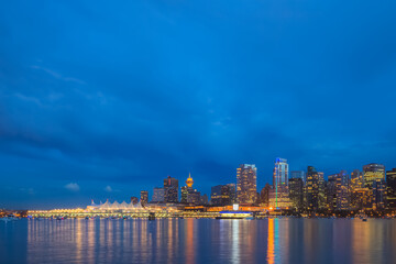Urban illuminated cityscape skyline of downtown Vancouver, B.C. and Coal Harbour from Stanley park seawall at night during blue hour.