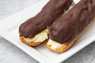 Chocolate eclair with a custard cream filling on a white plate.  With a concrete background