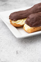 Chocolate eclair with a custard cream filling on a white plate.  With a concrete background