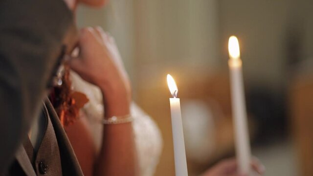 Newlyweds. Elegant caucasian bride and the groom stand and pray in church, holding candles in their hands. The wedding ceremony of the man and woman. Luxury bride in fashion dress. Slow motion