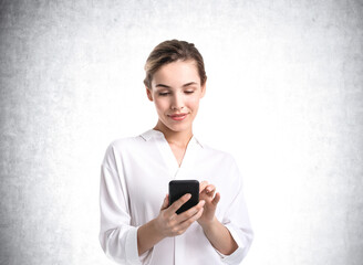 Businesswoman smiling with phone in hands, mockup empty wall