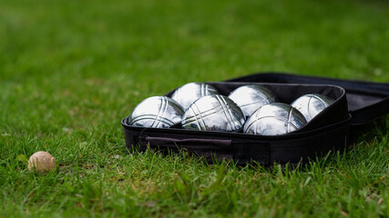 Petanque set with six metal balls in a black case on green grass. Play in your own garden during quarantine.