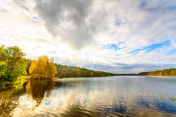 Sunset in the cloudy sky over the forest lake. View from the shore level