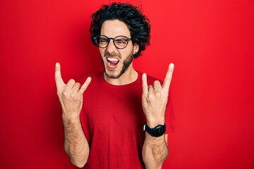 Handsome hispanic man wearing casual t shirt and glasses shouting with crazy expression doing rock symbol with hands up. music star. heavy concept.