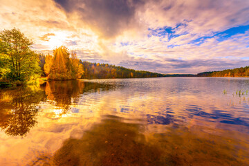 Sunset in the cloudy sky over the forest lake. View from the shore level
