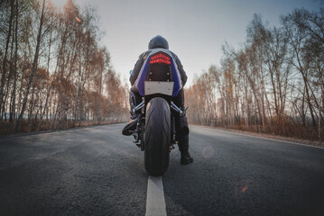 A motorbiker is ready to ride on the asphalt road. Rear view.