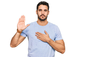 Young hispanic man wearing casual clothes swearing with hand on chest and open palm, making a...