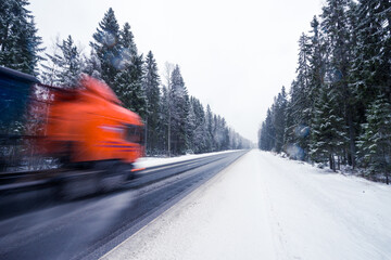 The truck is driving along the winter road during the snowfall passing through the spruce forest....