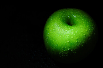 Green apple with water drops on a black background close-up