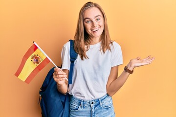 Beautiful blonde woman exchange student holding spanish flag celebrating achievement with happy smile and winner expression with raised hand