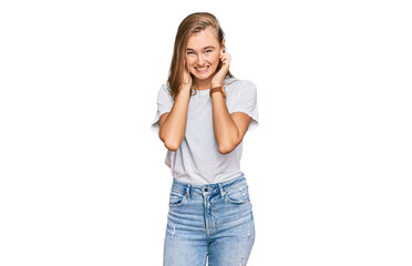 Beautiful young blonde woman wearing casual white t shirt covering ears with fingers with annoyed expression for the noise of loud music. deaf concept.