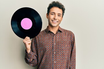Young handsome man holding vinyl disc looking positive and happy standing and smiling with a...
