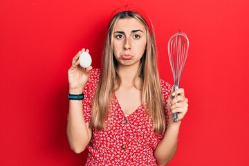 Beautiful hispanic woman holding egg and baker whisk depressed and worry for distress, crying angry and afraid. sad expression.