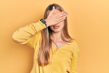 Beautiful hispanic woman wearing casual yellow sweater covering eyes with hand, looking serious and sad. sightless, hiding and rejection concept