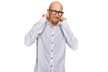 Bald man with beard wearing business shirt and glasses covering ears with fingers with annoyed expression for the noise of loud music. deaf concept.