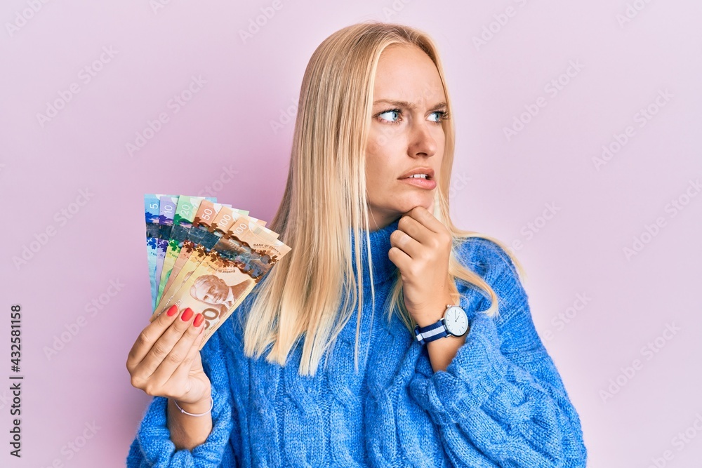 Canvas Prints Young blonde girl holding canadian dollars thinking worried about a question, concerned and nervous with hand on chin