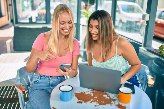 Two beautiful and young girl friends meeting at cafeteria using laptop and smartphone