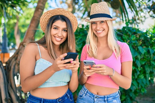 Two beautiful and young girl friends together having fun at the city using smartphone