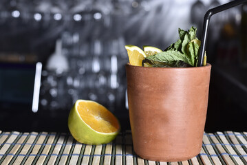 refreshing alcoholic drink with green fruits, ice vodka and gin, lemon peel served in clay glass on the counter on blurred background