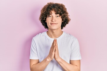 Handsome young man wearing casual white t shirt praying with hands together asking for forgiveness smiling confident.
