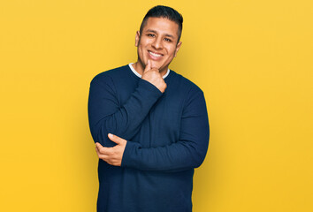Fototapeta premium Young latin man wearing casual clothes looking confident at the camera with smile with crossed arms and hand raised on chin. thinking positive.