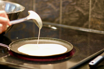 pouring batter with ladle for the crepe on the hot frying pan. Traditional cooking technique - obrazy, fototapety, plakaty