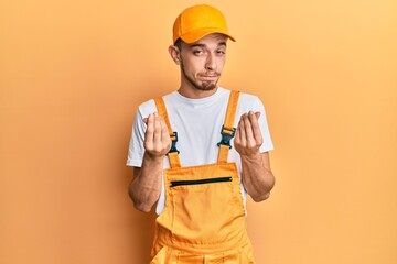 Hispanic young man wearing handyman uniform doing money gesture with hands, asking for salary...