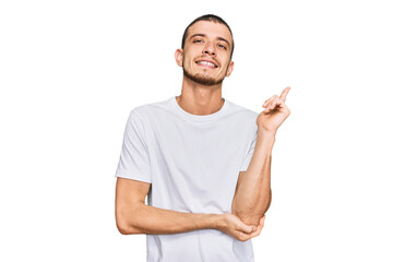 Hispanic young man wearing casual white t shirt with a big smile on face, pointing with hand and finger to the side looking at the camera.