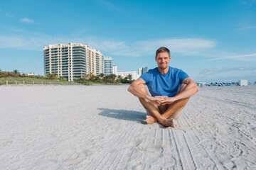 Fototapeta na wymiar Guy walking along the empty sandy Miami beach. Happy handsome man tourist in casual clothes sitting on sandy beach. Travel and tourism concept.