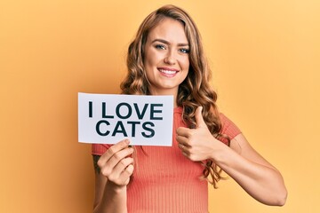 Fototapeta na wymiar Young blonde girl holding paper with i love cats phrase smiling happy and positive, thumb up doing excellent and approval sign